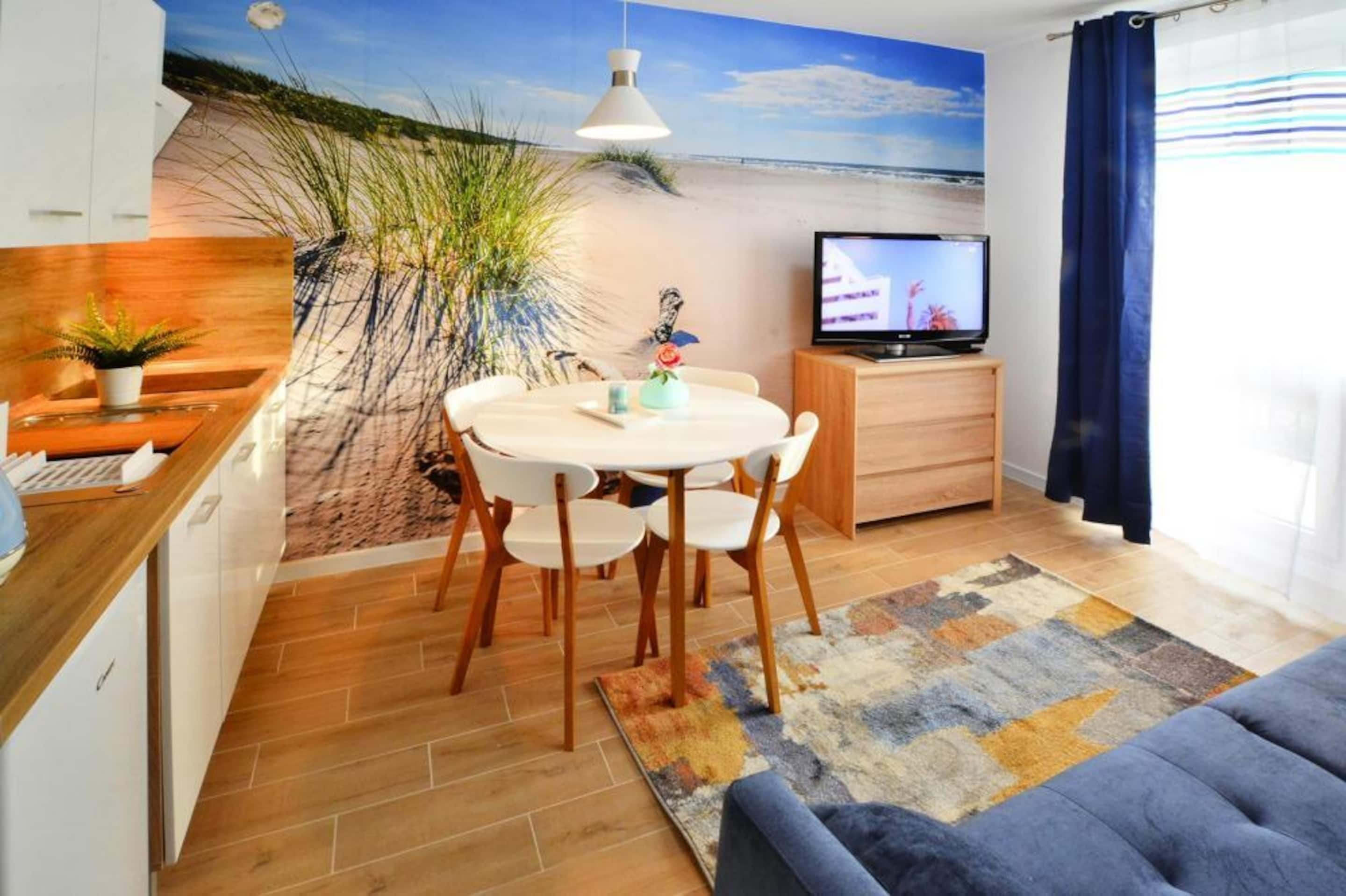 Ett vardagsrum med en väggmålning som föreställer en strand, ett runt matbord med stolar, en tv och en soffa.