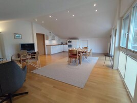 A modern apartment with a living room, dining area, kitchenette, and large windows.