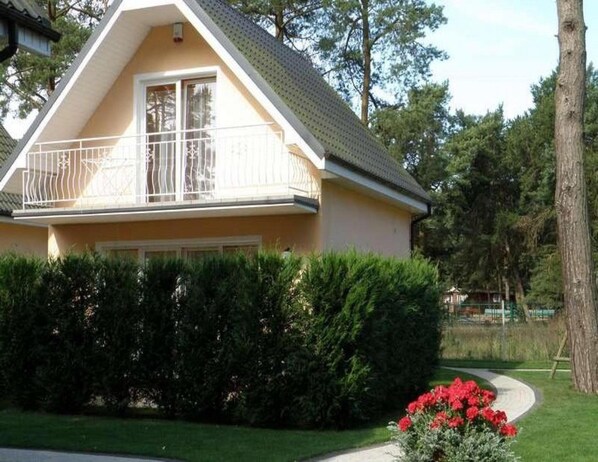 A two-story house with a balcony, surrounded by a well-maintained hedge and a small garden with red flowers. - Large, Comfortable Holiday Homes Close to the sea (Rewal)