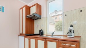 Une cuisine compacte avec des meubles en bois, une cuisinière encastrée, une machine à café et une fenêtre donnant sur des immeubles.