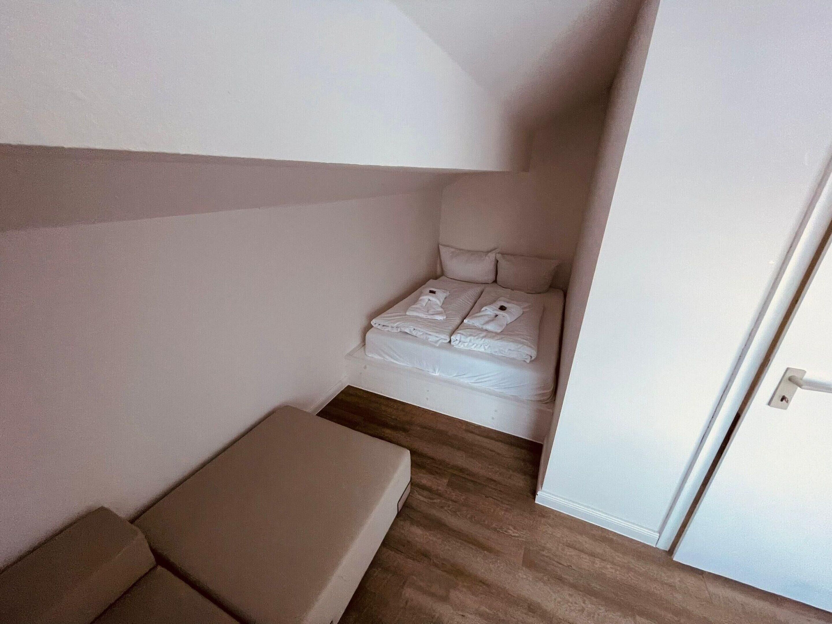 A small, clean room with a bed, a bench, and a door.