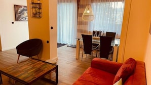 A living room with a red sofa, a black chair, and a wooden coffee table. There is a dining area with a table and chairs in the background. - Ferienhaus im Kurort Inkl. Fruhstuck (Goslar)