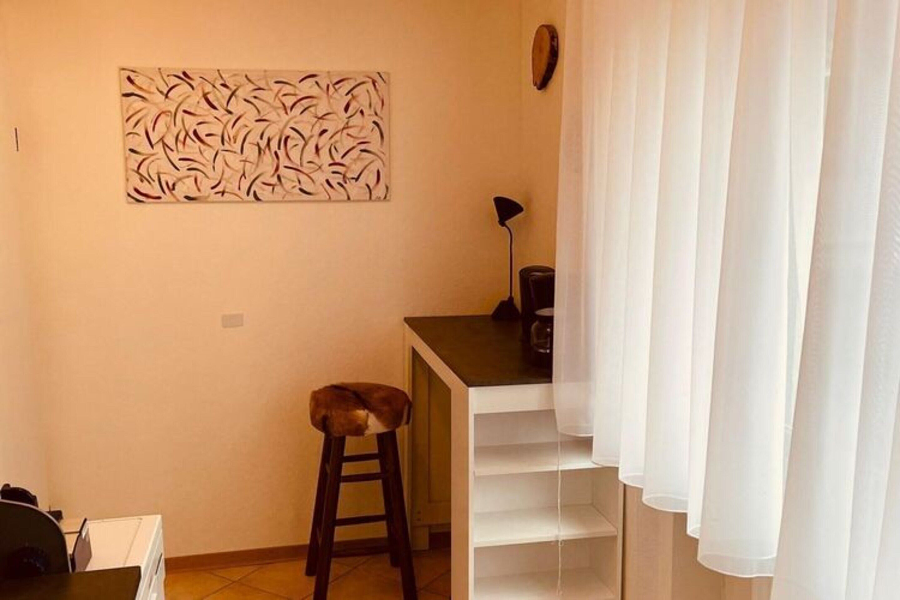A small, compact room with a kitchenette, a stool, a table, and a white curtain.