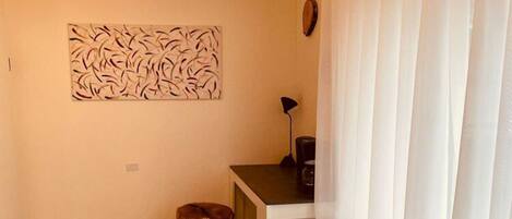 A small, compact room with a kitchenette, a stool, a table, and a white curtain.