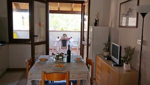 Comedor con mesa lista para cuatro personas, un televisor sobre un mueble de madera y una ventana con cortinas.