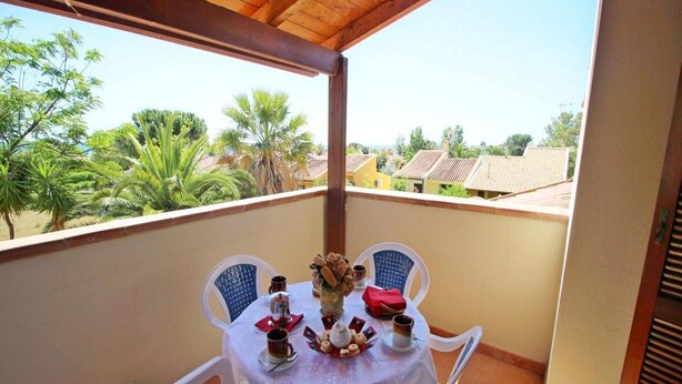 Un balcón con mesa lista para dos personas, sillas y vistas a una zona residencial con palmeras y casas.