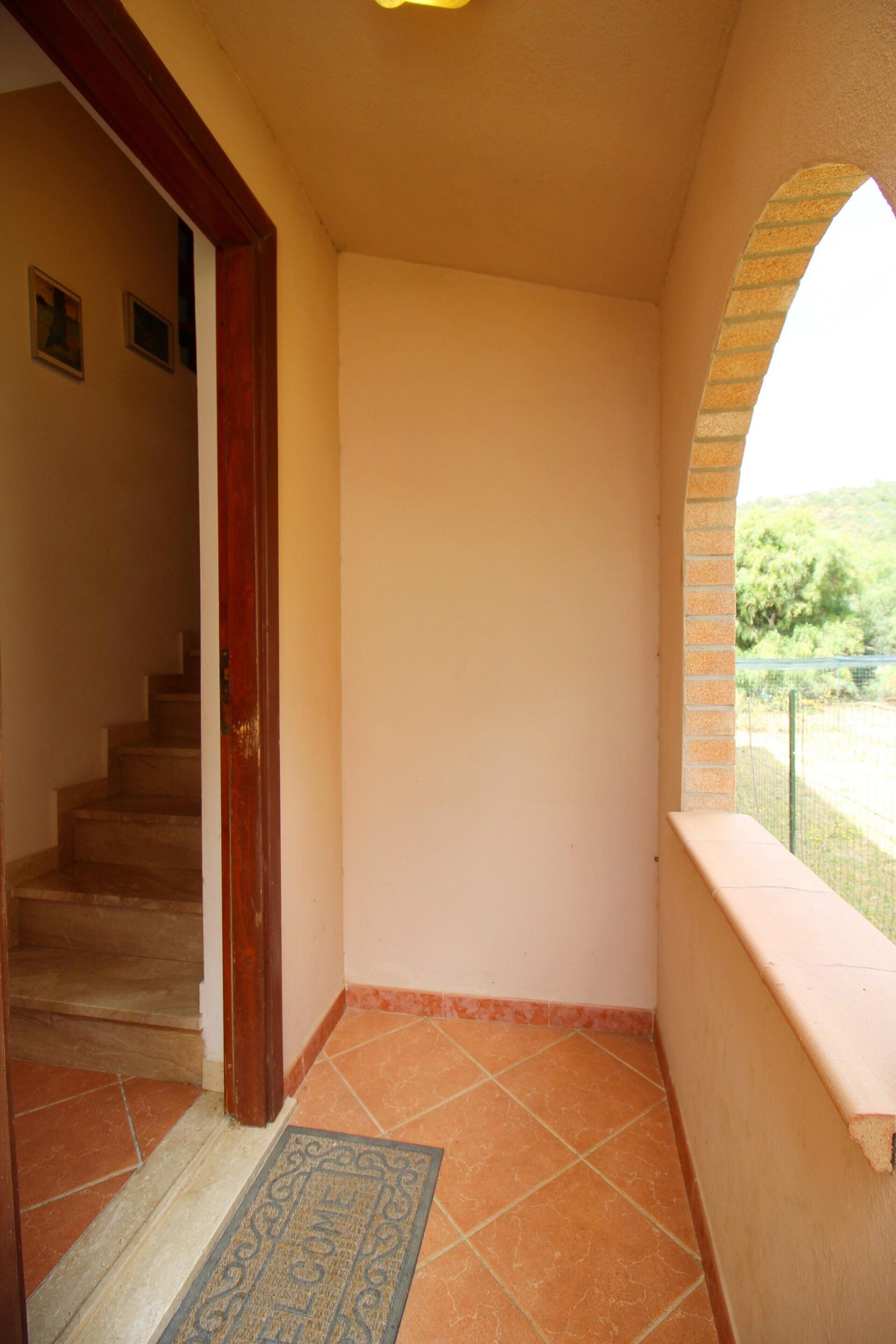 Un corridoio con pavimento piastrellato, una porta in legno e una vista attraverso una finestra ad arco.