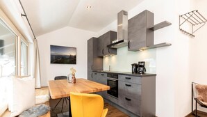 A modern kitchen with grey cabinets, a wooden dining table, and a yellow chair. - Penthouse in Strass Near Zillertal Alps (Strass im Zillertal)