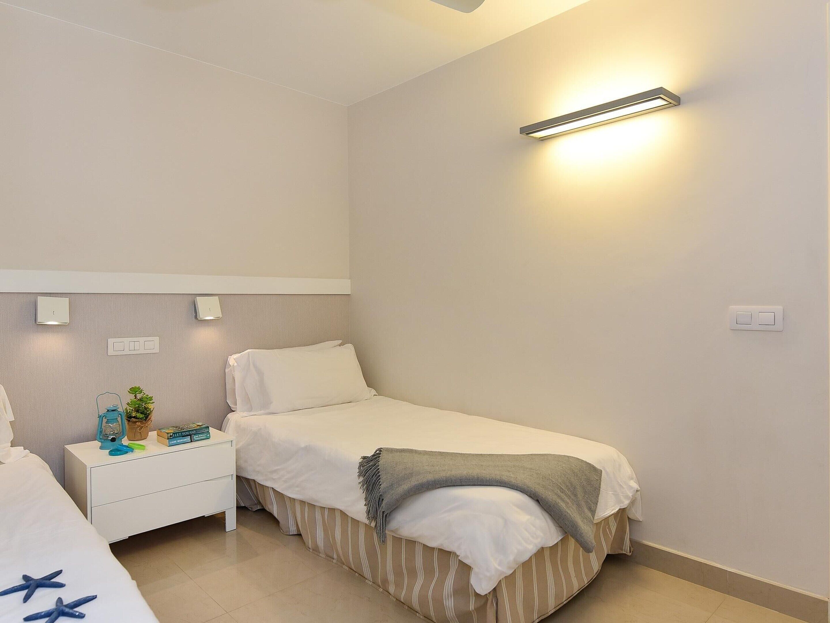 A bedroom with a single bed, a bedside table with a lamp, and a wall-mounted light fixture.