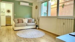 Un salón con un sofá color beige, un tapete redondo y una ventana con vistas a un edificio.