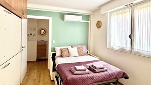 Un dormitorio con cama, ventana con cortinas, un reloj y una puerta que da a otra habitación.