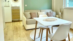 Una sala de estar moderna con un sofá blanco, una mesa de comedor con sillas, piso de madera y una pared de acento verde.