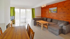 A modern living room with a wooden wall, a grey sofa, a wooden coffee table, and a dining table with chairs. - Comfortable Holiday Home With a Private Garden (Mielno)