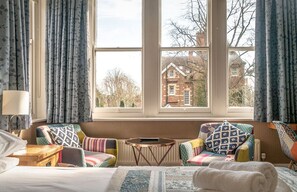 A cozy room with a large window, a bed, a small table, and two colorful armchairs. - 100 Banbury road Oxford (Oxford)