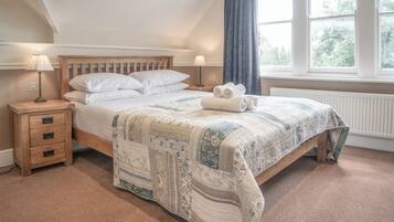 A bedroom with a wooden bed, two bedside tables, a quilt, and a view of trees through a window.