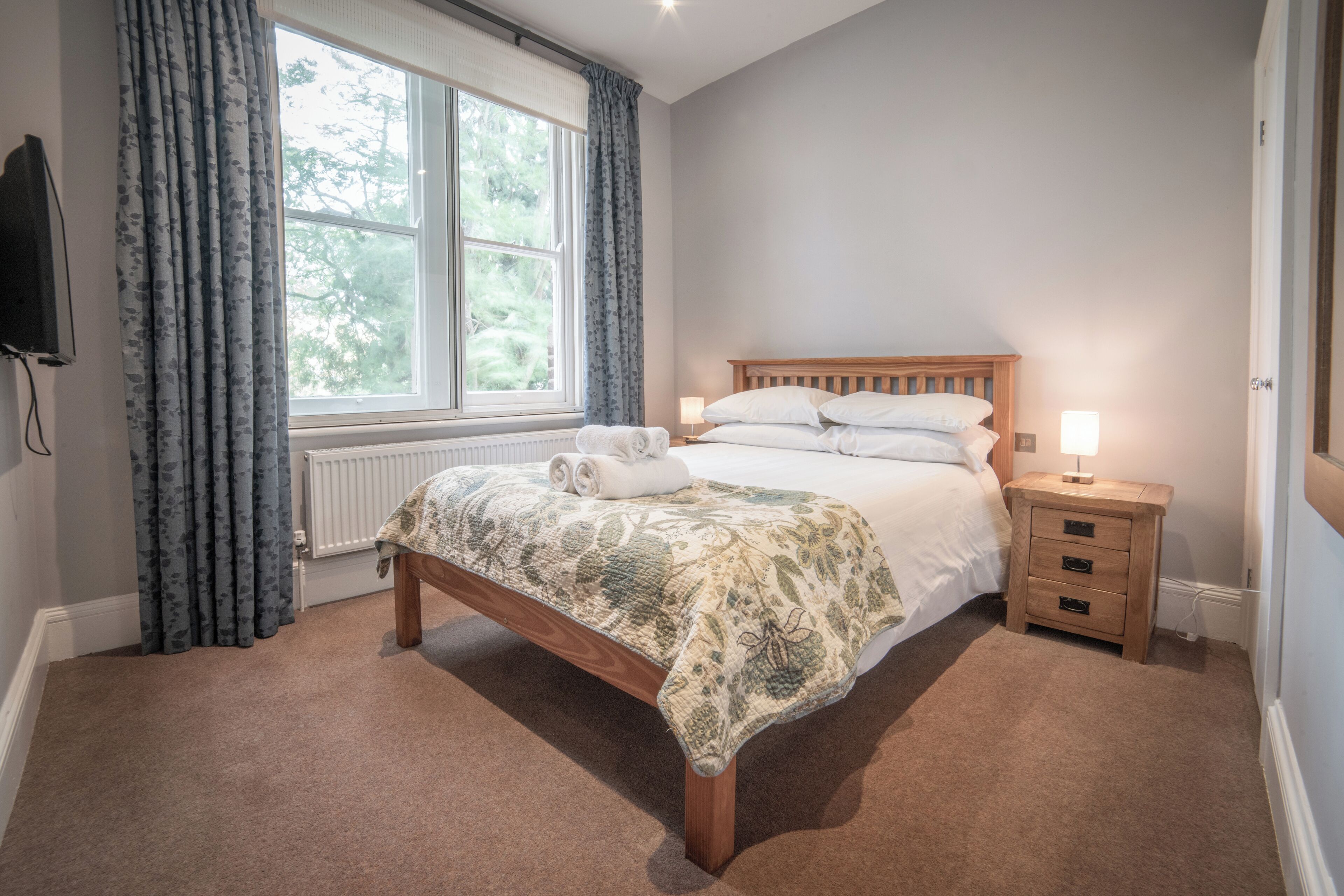Une chambre à coucher avec un lit en bois, une table de chevet avec une lampe, un radiateur et une fenêtre avec des rideaux.
