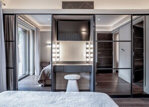 A modern bedroom with a large bed, a vanity with lights, and a walk-in closet.