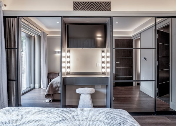A modern bedroom with a large bed, a vanity with lights, and a walk-in closet.