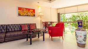 A modern living room with a dark brown sofa, a red armchair, a glass coffee table, and a large vase. - Mai Villa Ngan Son HN - by BAY LUXURY (Hanoi)