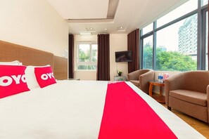 A hotel room with a large bed, a TV, a sofa, and a window with a view of greenery and buildings. - Mai Villa Ngan Son HN - by BAY LUXURY (Hanoi)