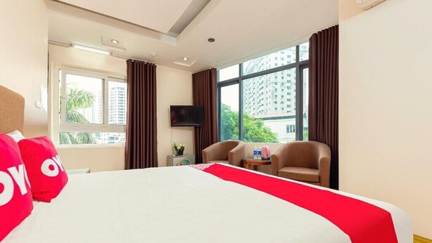 A hotel room with a large bed, two armchairs, a TV, and a window with a city view. - Mai Villa Ngan Son HN - by BAY LUXURY (Hanoi)