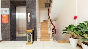 An elevator, a staircase with a red handrail, and potted plants in a lobby area. - Mai Villa Ngan Son HN - by BAY LUXURY (Hanoi)