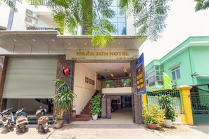 The entrance of Ngân Sơn Hotel with a staircase leading to the upper floor, potted plants, and a closed garage door. - Mai Villa Ngan Son HN - by BAY LUXURY (Hanoi)