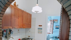 A kitchen with wooden cabinets, a gas stove, a sink, and a red refrigerator. - Adriano's beach house (Anzio)