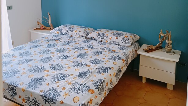 A bedroom with a bed, a nightstand, a wall-mounted compass, and a hanging light fixture. - Adriano's beach house (Anzio)