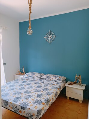 A bedroom with a bed, a nightstand, a wall-mounted compass, and a hanging light fixture. - Adriano's beach house (Anzio)