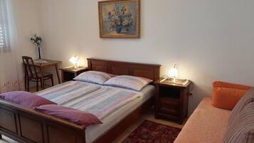 A bedroom with a bed, bedside tables with lamps, a desk with a chair, a painting on the wall, and a sofa.