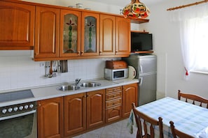 Compact kitchen with a stainless steel sink, microwave, and refrigerator, plus a wooden table and chair.