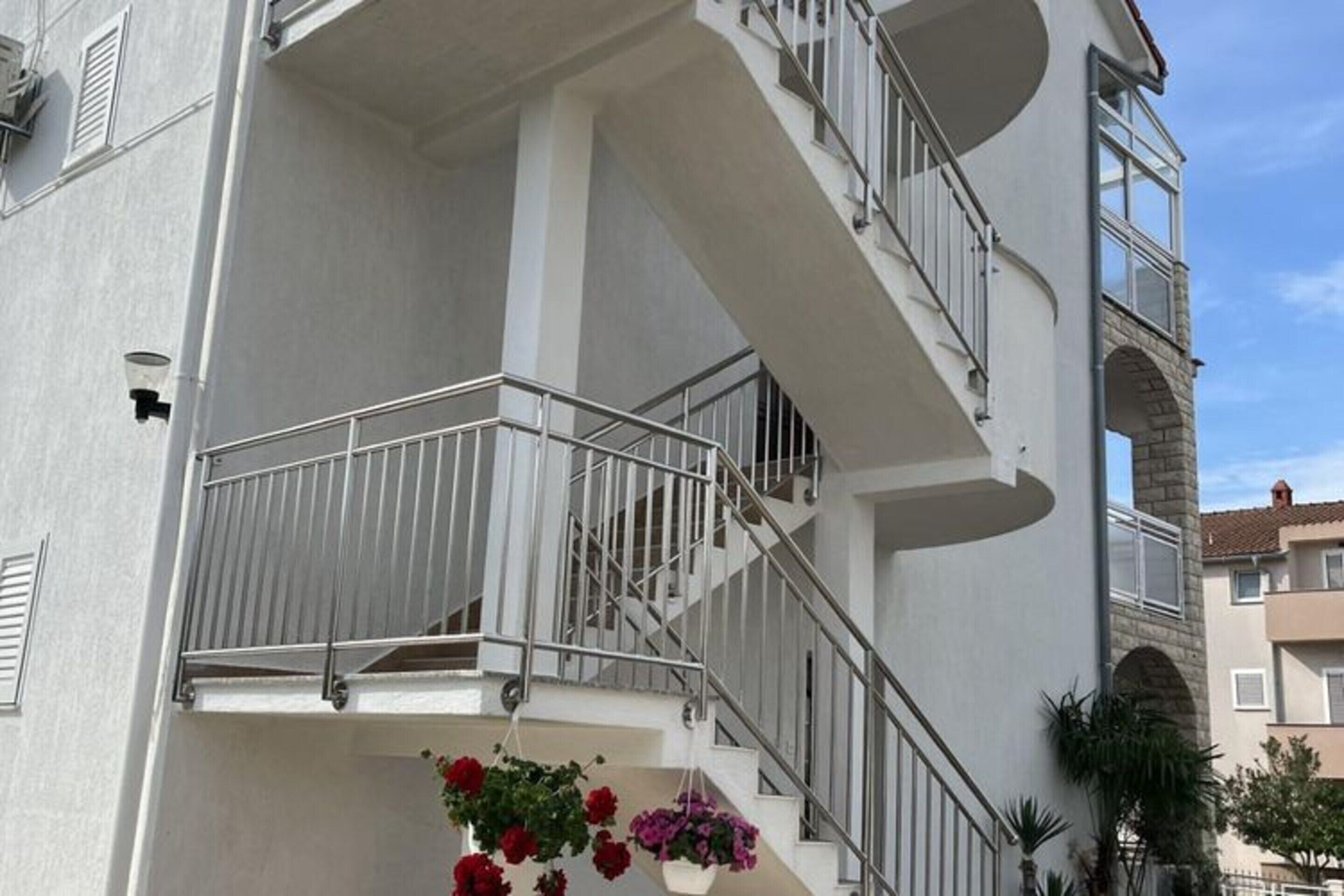 Un immeuble à plusieurs étages, à la façade blanche, doté d’un escalier en métal et de jardinières suspendues.