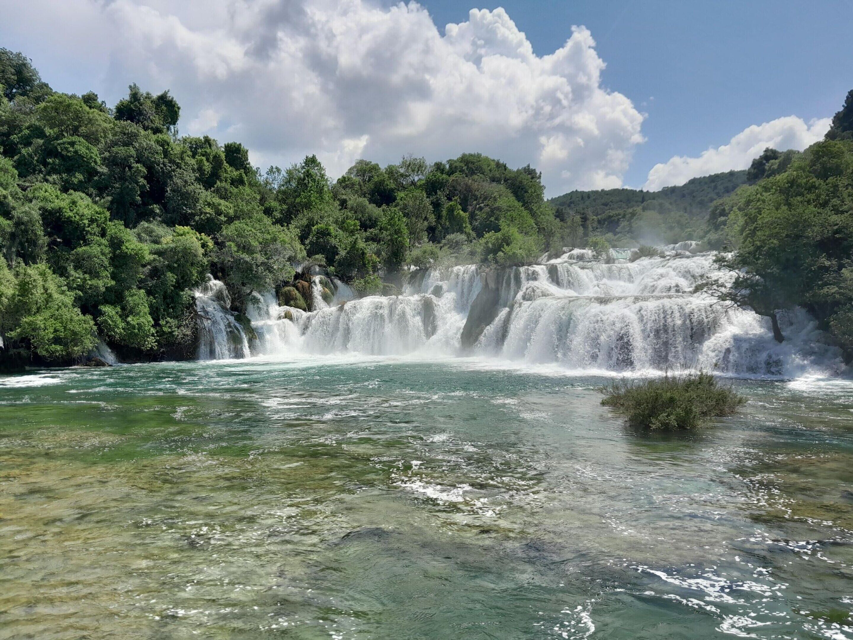 Ein Wasserfall stürzt in einen Fluss, umgeben von dichtem Grün.
