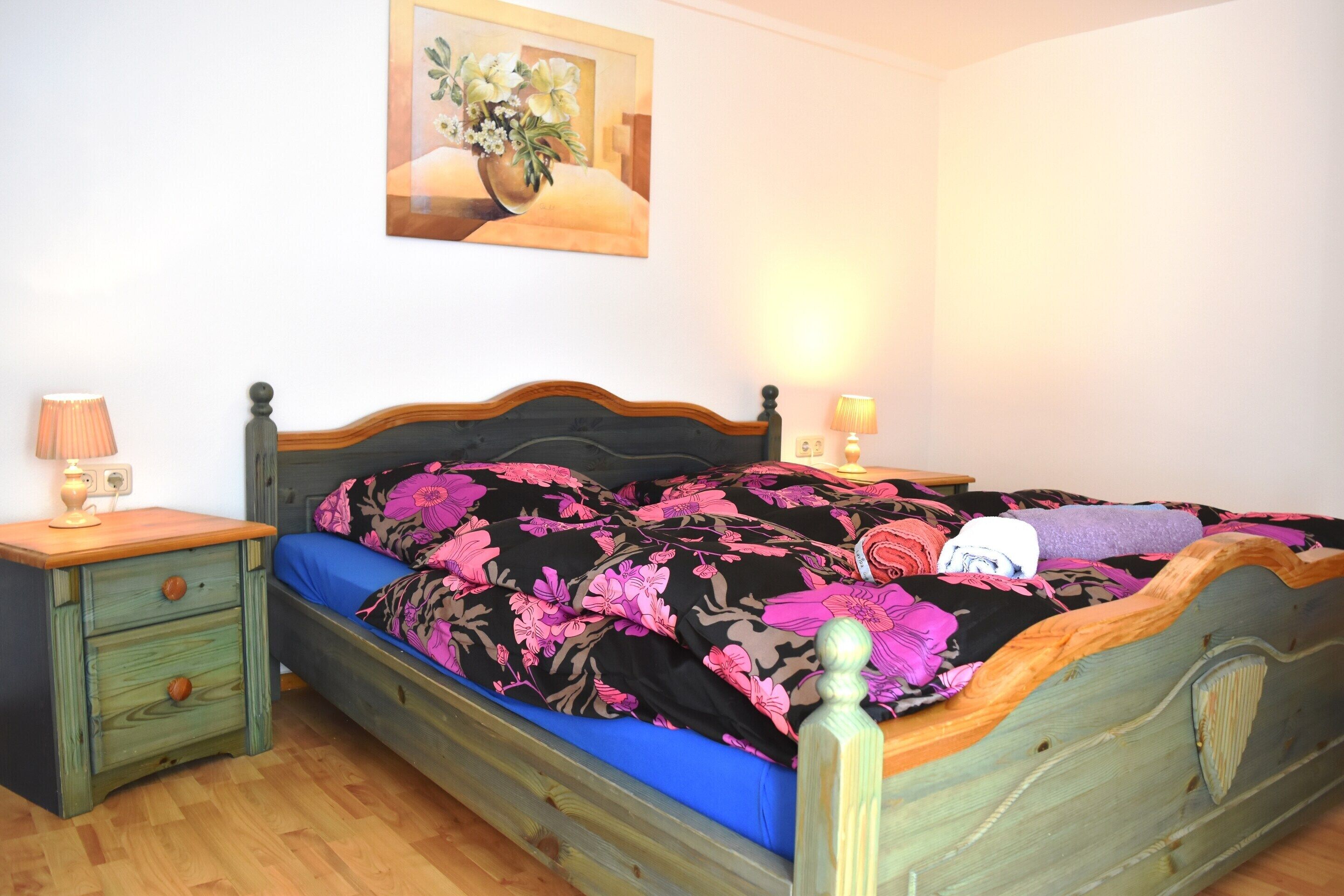 Ein Schlafzimmer mit einem hölzernen Bett, einem Nachttisch, einer Lampe und einem Bild an der Wand.