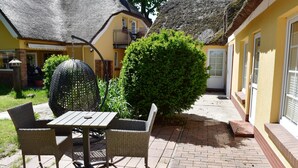 Une terrasse avec une table et des chaises, un objet décoratif de forme sphérique et une haie bien entretenue.