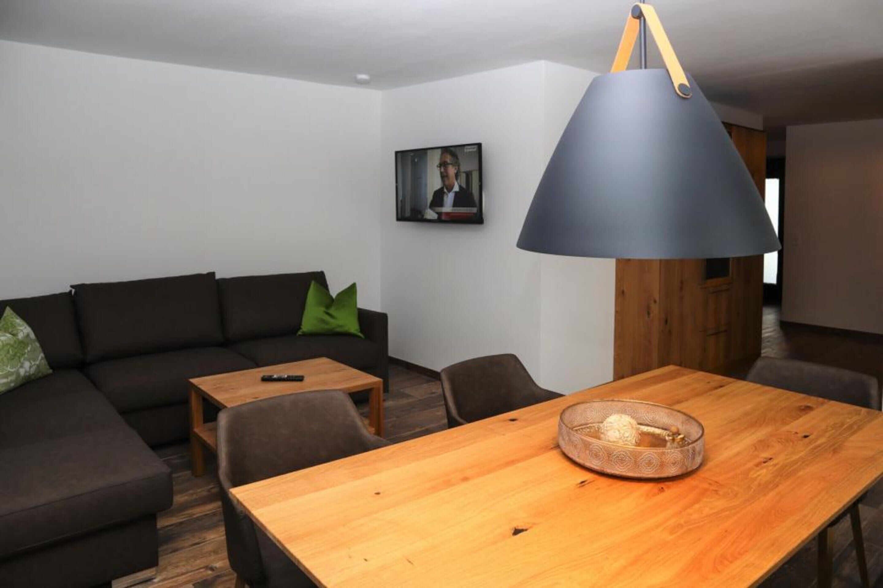 A modern living room with a wooden dining table, a black sofa with green cushions, and a large floor lamp.