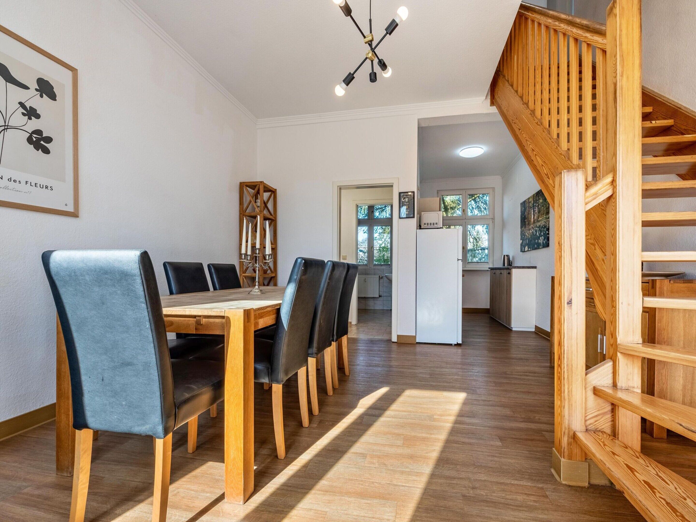 Ein Essbereich mit Holztisch und Stühlen, einer Chandelierleuchtre und einer Treppe.