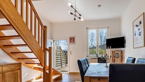 A dining area with a wooden staircase, a dining table with chairs, a TV mounted on the wall, and a window with a view of the outside. - Komfortables XXL Reihenhaus mit Wlan in Buchholz (Buchholz)