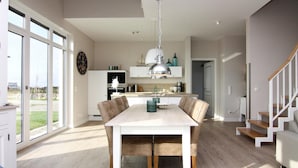 A modern kitchen with a dining area, large windows, and a staircase. - Ferienhaus Klint in Lancken (Dranske)