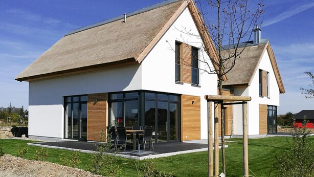 A modern two-story house with a large glass front, wooden shutters, and a thatched roof. - Ferienhaus Klint in Lancken (Dranske)