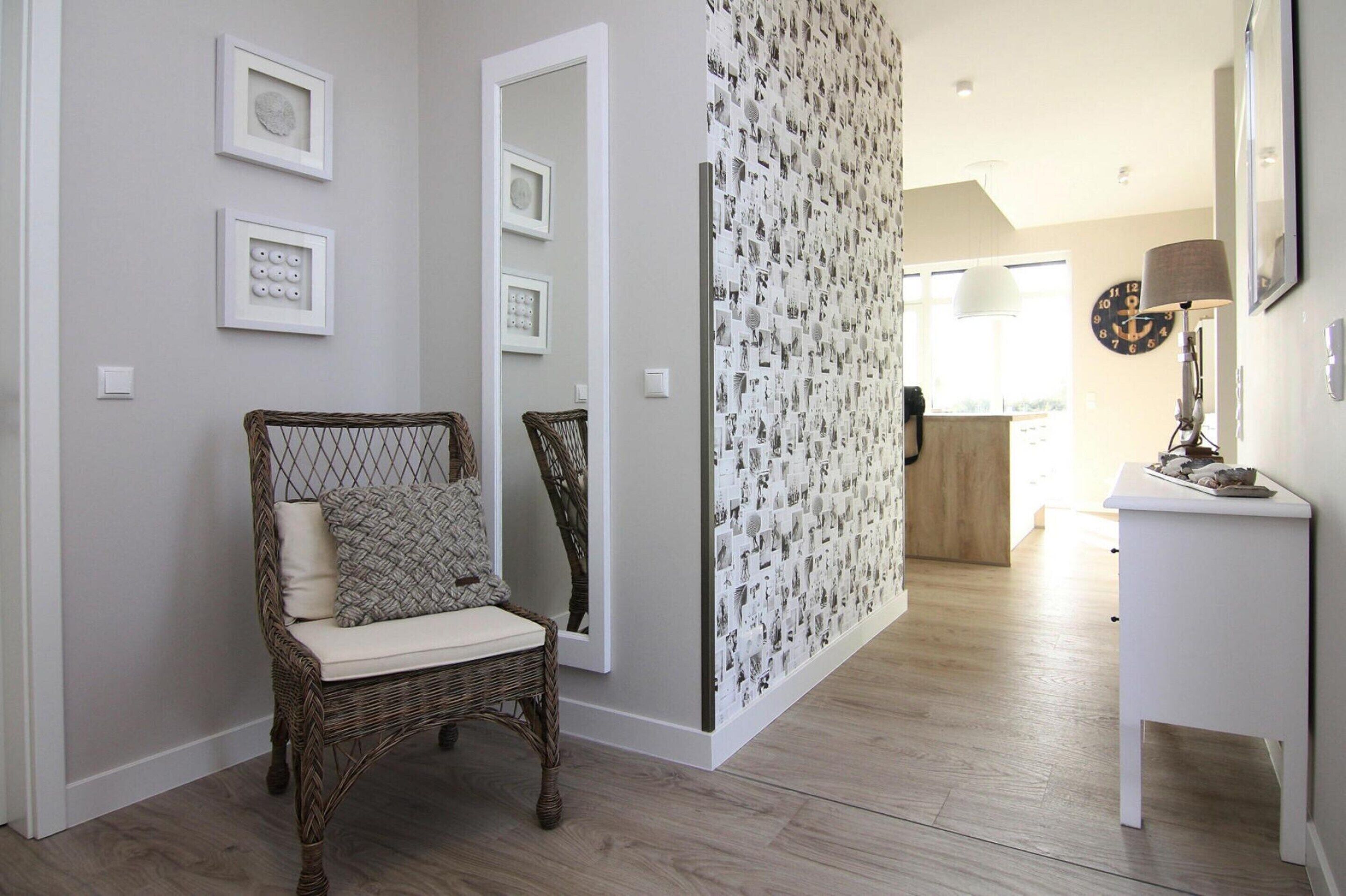 A hallway with a wicker chair, framed pictures, a patterned wall, and a lamp on a side table.