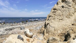 A rocky beach with a large mound of sand and scattered rocks. - Ferienhaus Klint in Lancken (Dranske)