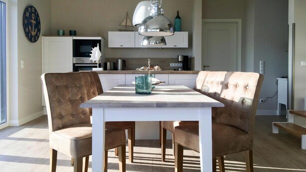 A dining area with a white table and two brown upholstered chairs. - Ferienhaus Klint in Lancken (Dranske)