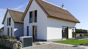 A modern two-story house with a sloped roof, large windows, and a stone wall. - Ferienhaus Klint in Lancken (Dranske)