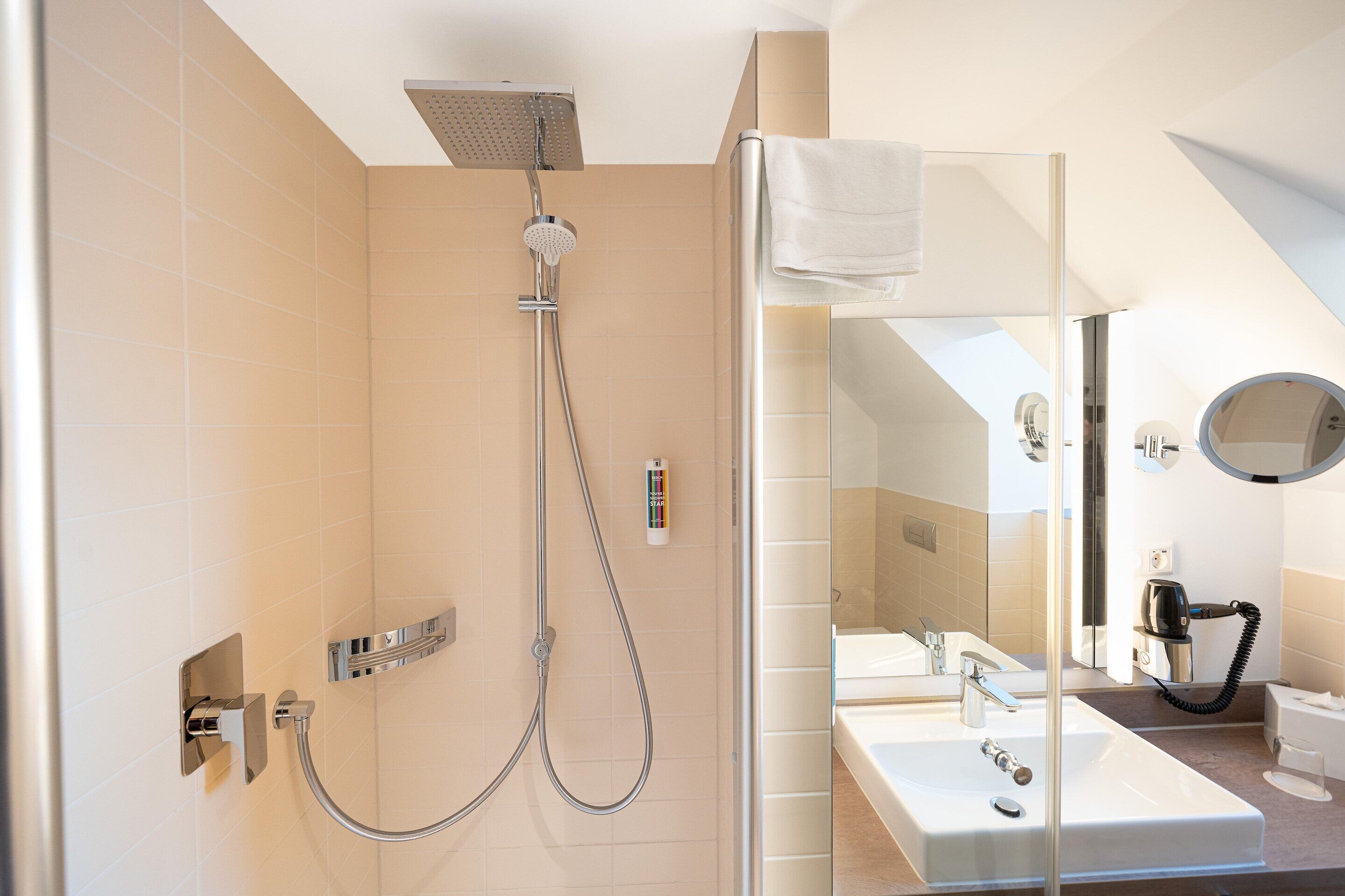 Un baño moderno con ducha envuelta en vidrio, un espejo grande y una zona separada para el lavamanos.