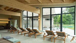 Une pièce baignée de lumière naturelle, avec des poutres en bois, de grandes fenêtres et un espace au bord de la piscine équipé de chaises longues.