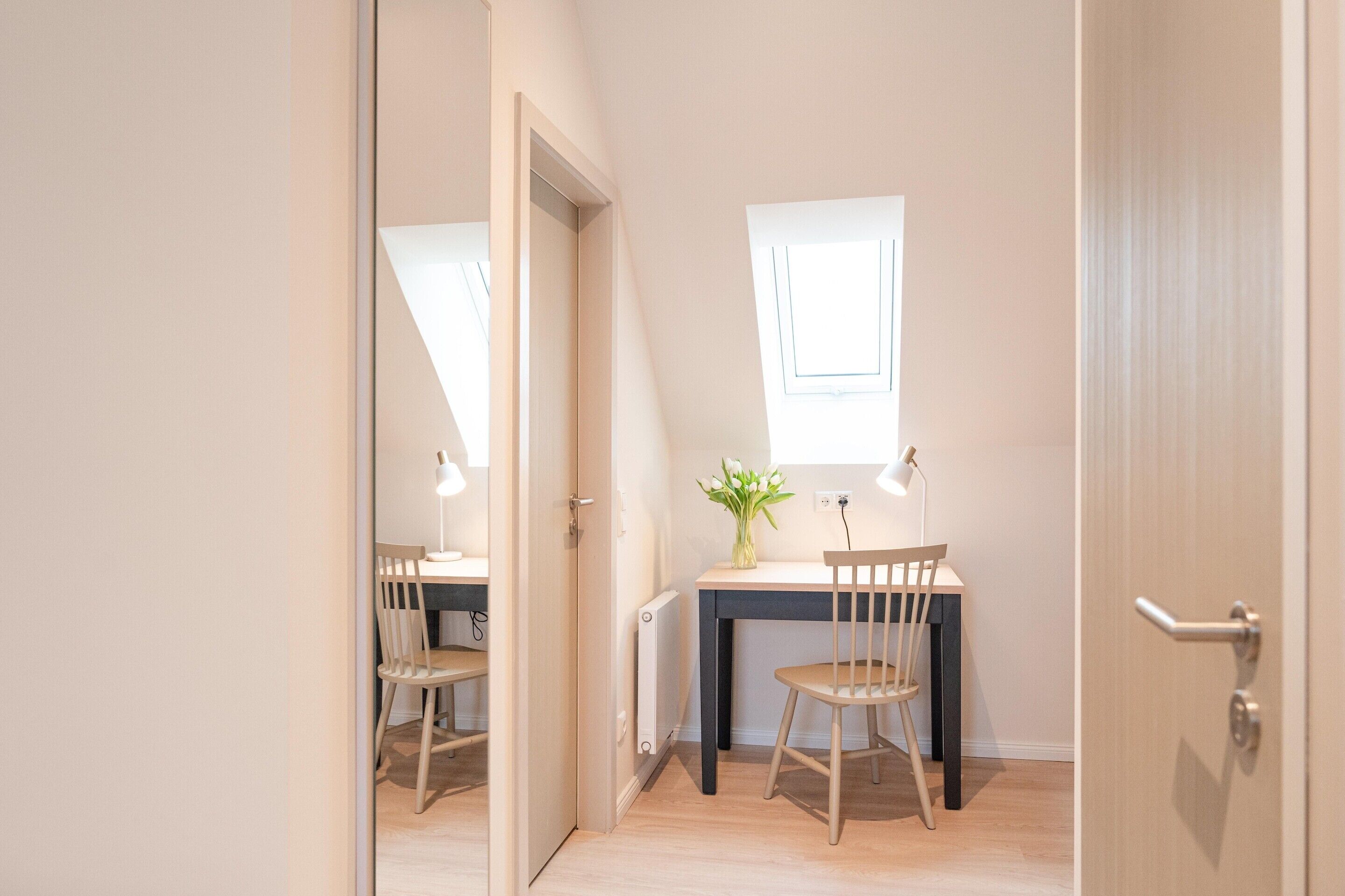 Una habitación moderna y luminosa con un escritorio, dos sillas, una planta pequeña y una ventana.