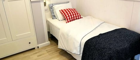 Un dormitorio pequeño y ordenado con una cama individual, una mesita de noche, una lámpara y una puerta.