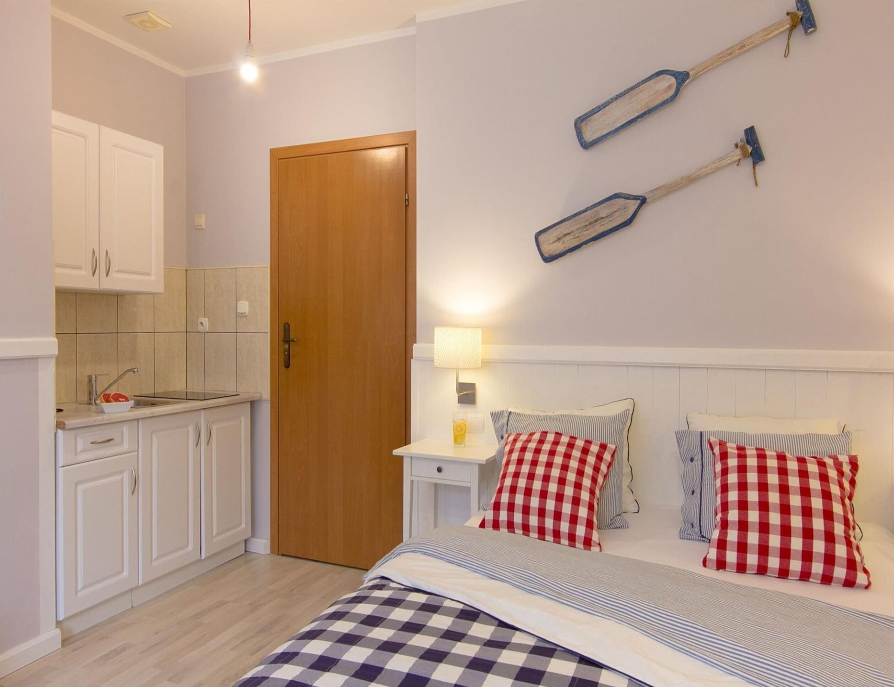 Une chambre avec une couvre-lit à carreaux, une table de chevet avec une lampe et une porte en bois.